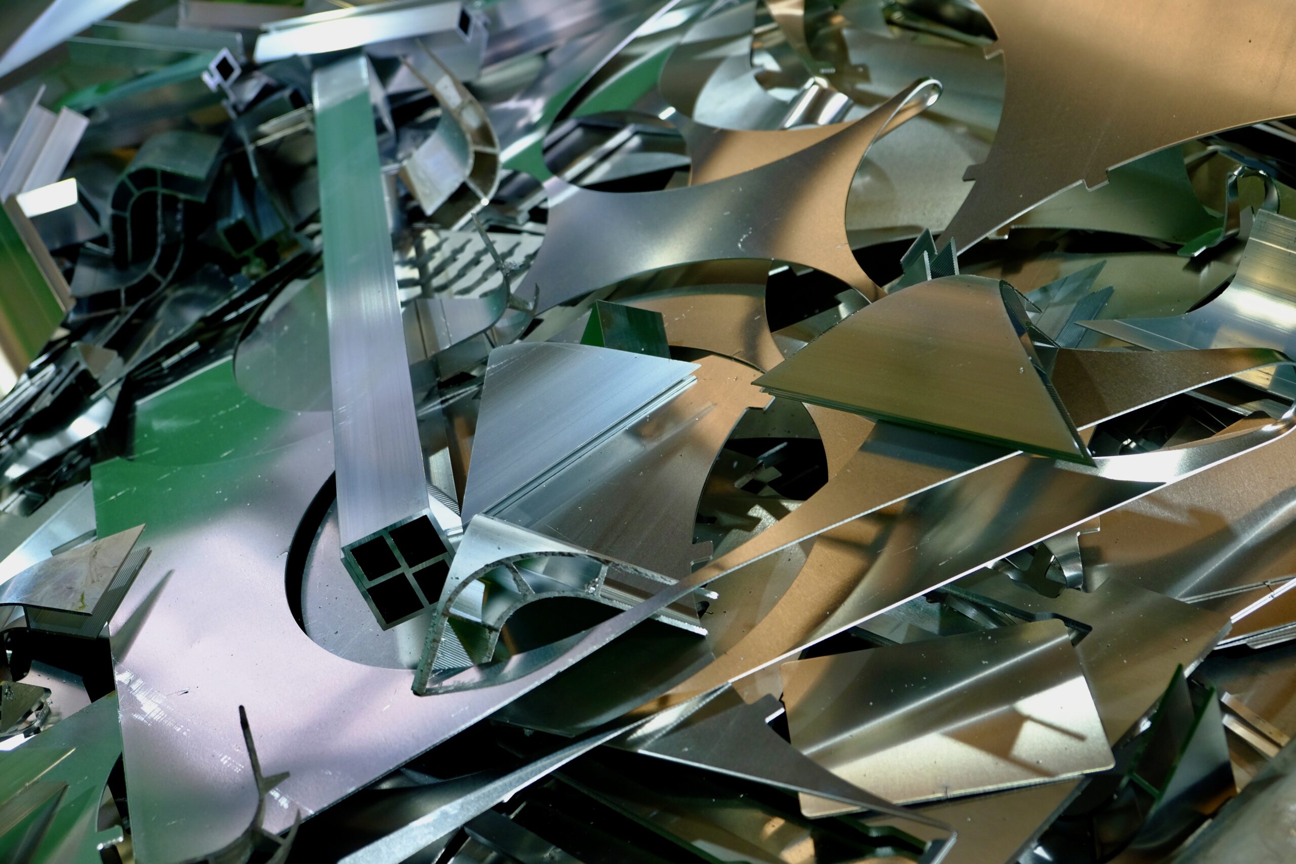 A pile of laser-cut offcut skeletons, curved and angular scrap in bright galvanised steel