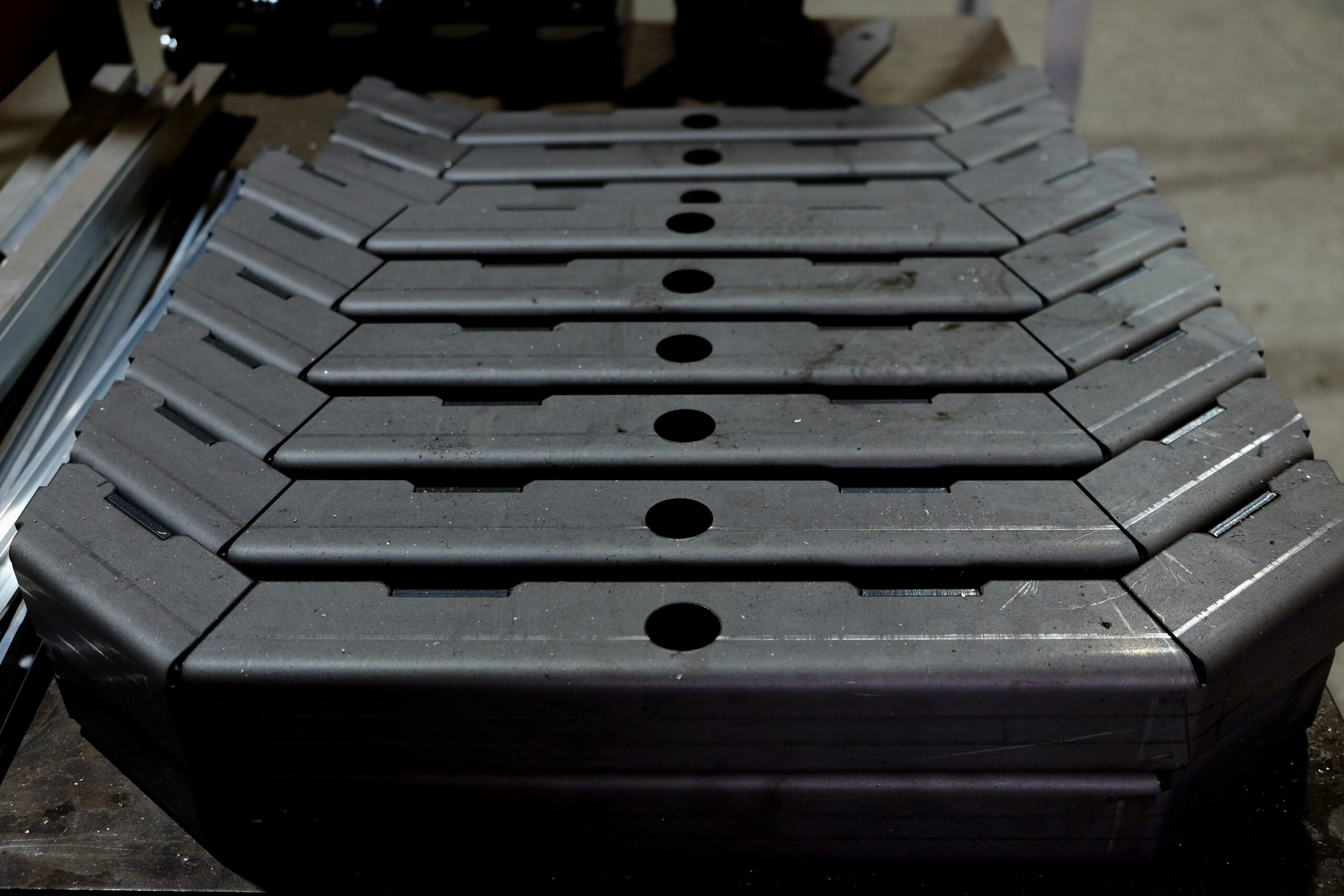 Formed steel parts stacked in a row, showing the bend radius and pierced holes on each