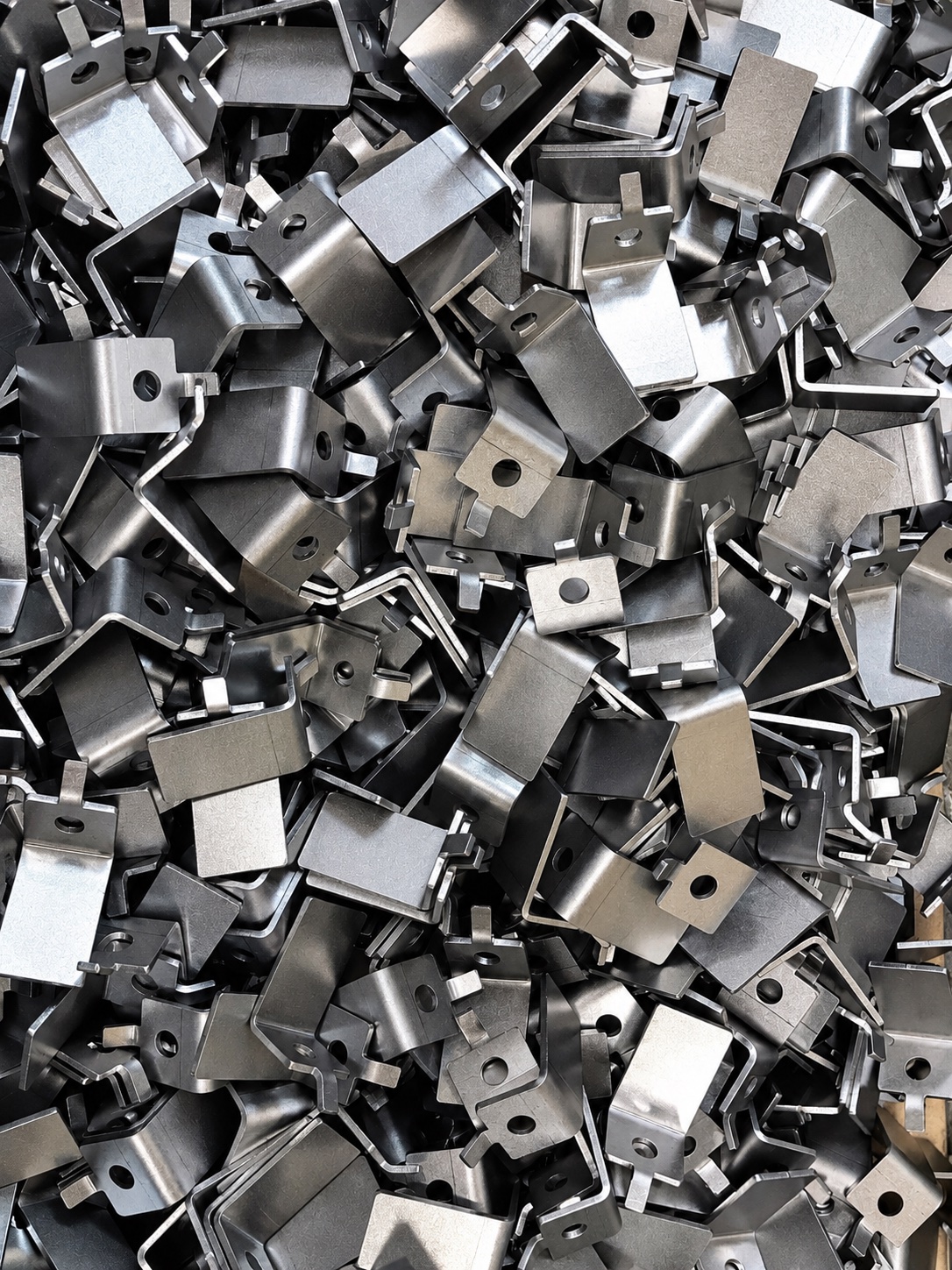 A dense pile of small formed steel brackets, each pierced and folded the same way