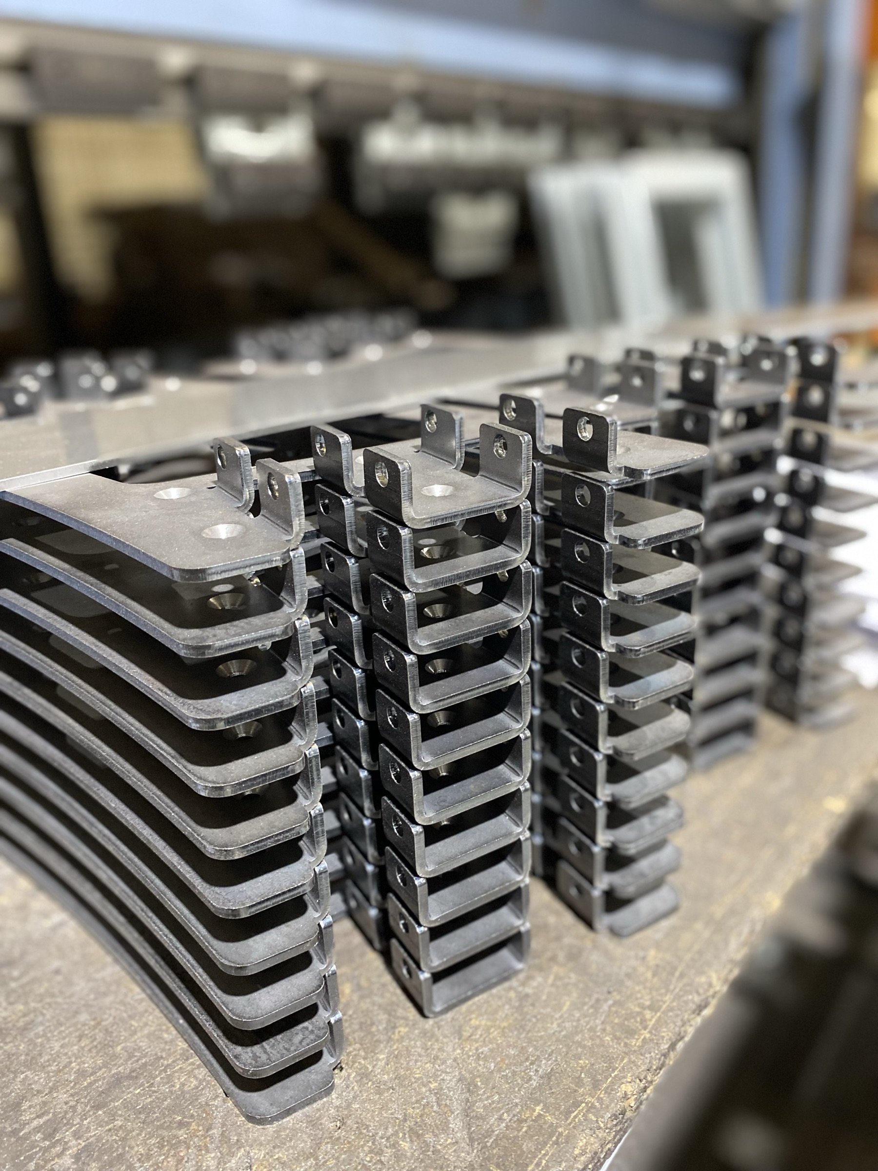 Stacks of laser-cut and formed steel brackets on the workshop bench, countersunk holes and folded tabs on each