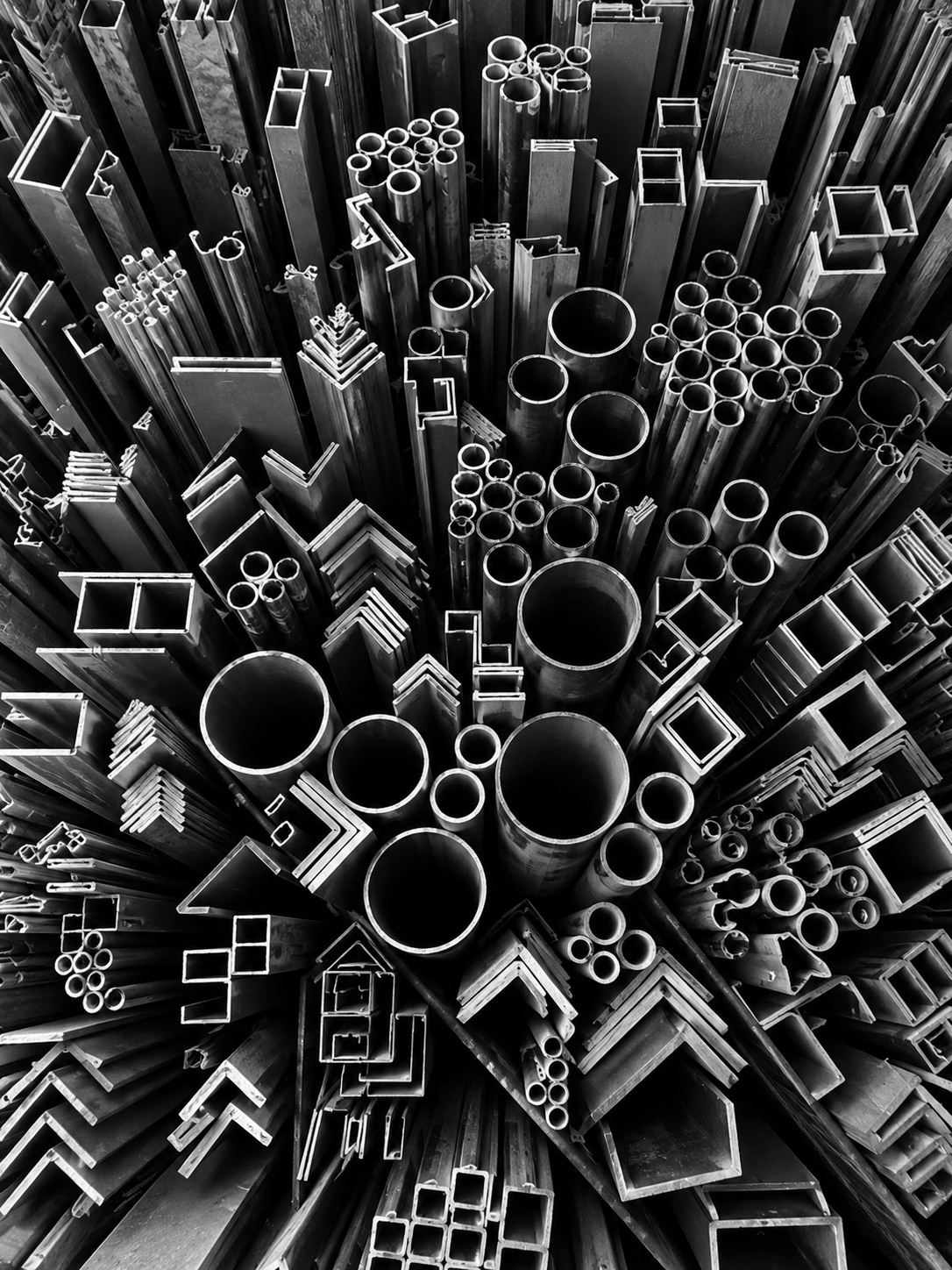 Looking down on the ends of stacked metal tube, box section and angle, in black and white
