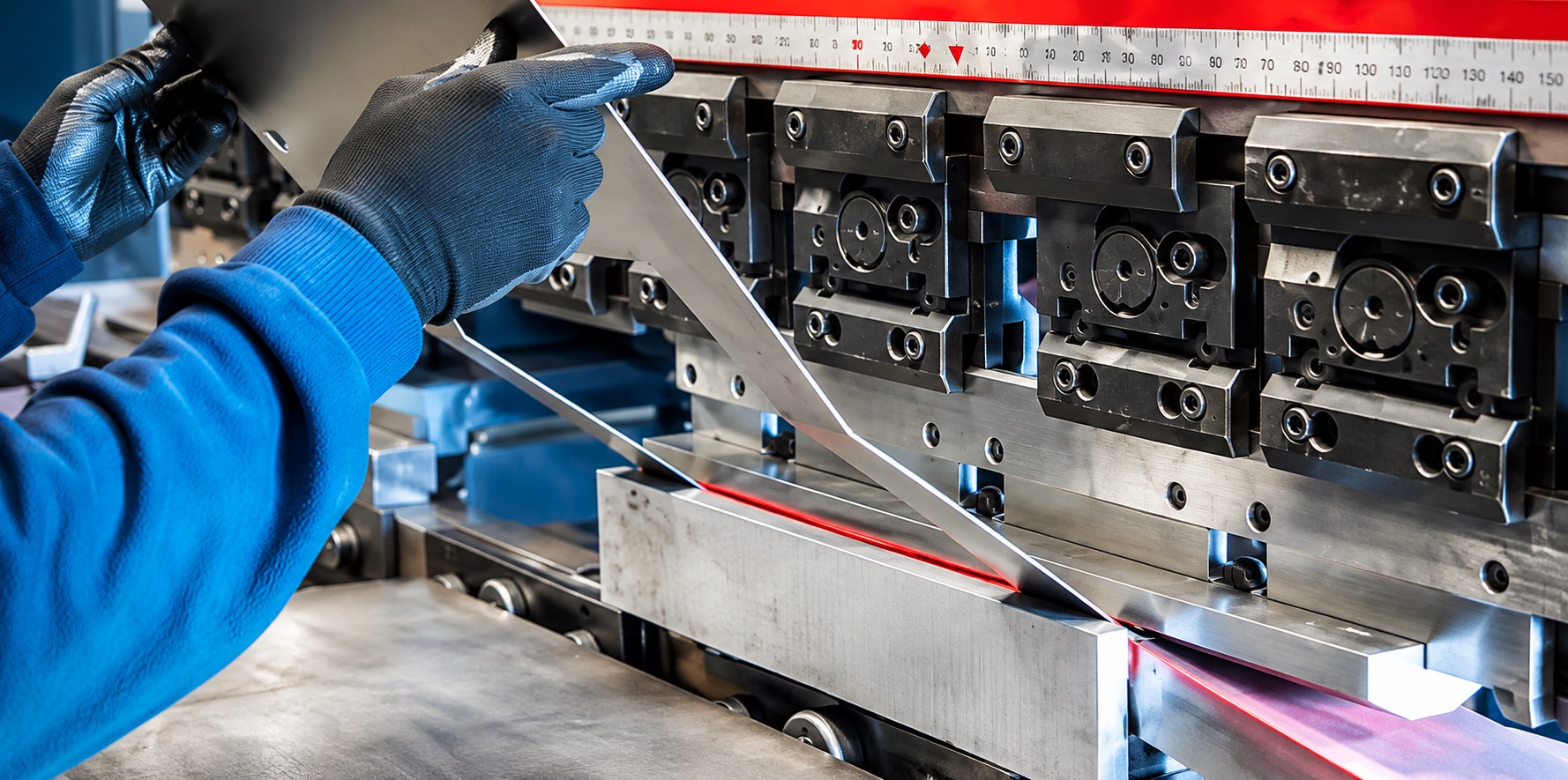 Gloved hands guiding a sheet of steel into the tooling of a CNC press brake