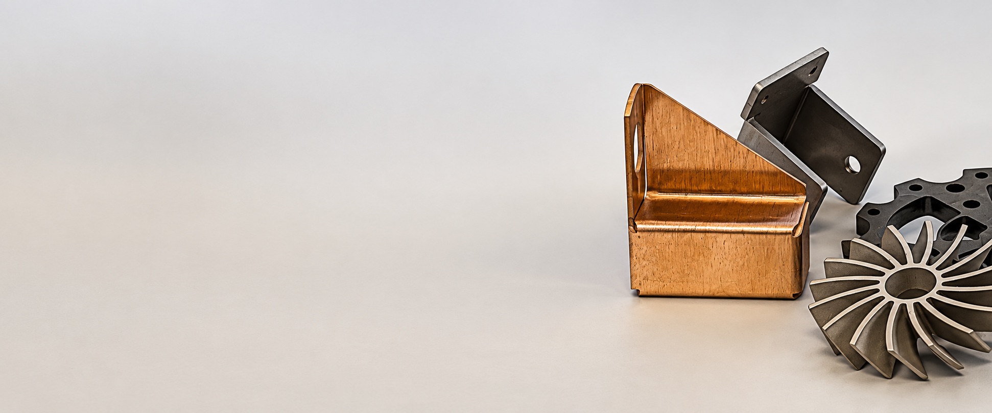 Small formed and profiled metal parts on a plain background, a folded copper bracket in front